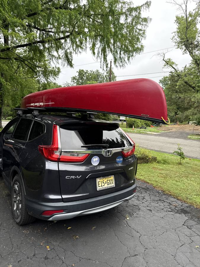The red Mad River canoe strapped to the roof of a grey Honda CR-V in a driveway.