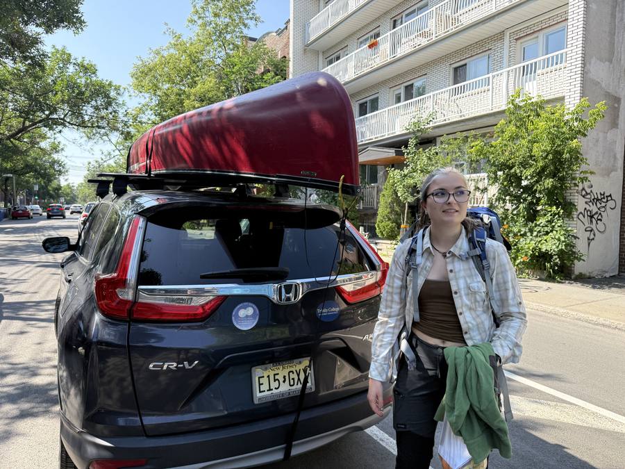 Violette standing beside the car and canoe on a Montréal street with a backpack on.