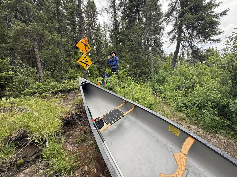 The empty canoe at a portage landing next to yellow SEPAQ portage and rapids signs.