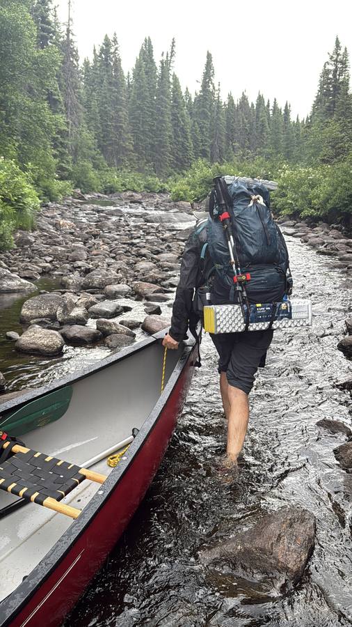 Lining the loaded canoe down a shallow rocky river.