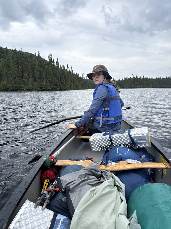 View from the stern of Violette paddling in the bow across an open lake under dramatic grey clouds.