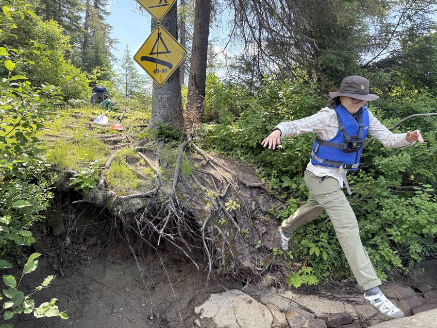 Violette mid-jump off a bank with exposed tree roots, a SEPAQ campsite sign above.