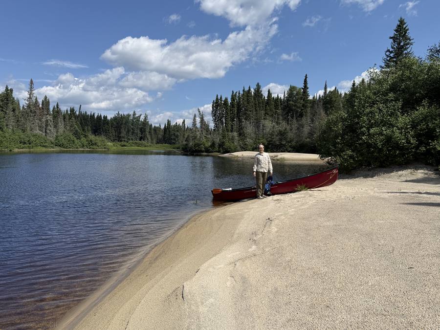 Stan beside the canoe on a sandy lakeshore beach.